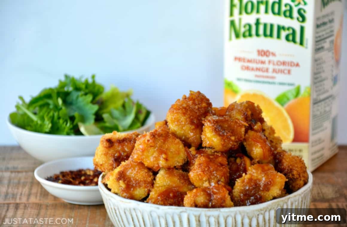 Crispy Citrus Chicken Bites 5 A white bowl containing orange chicken poppers with a carton of orange juice in the background