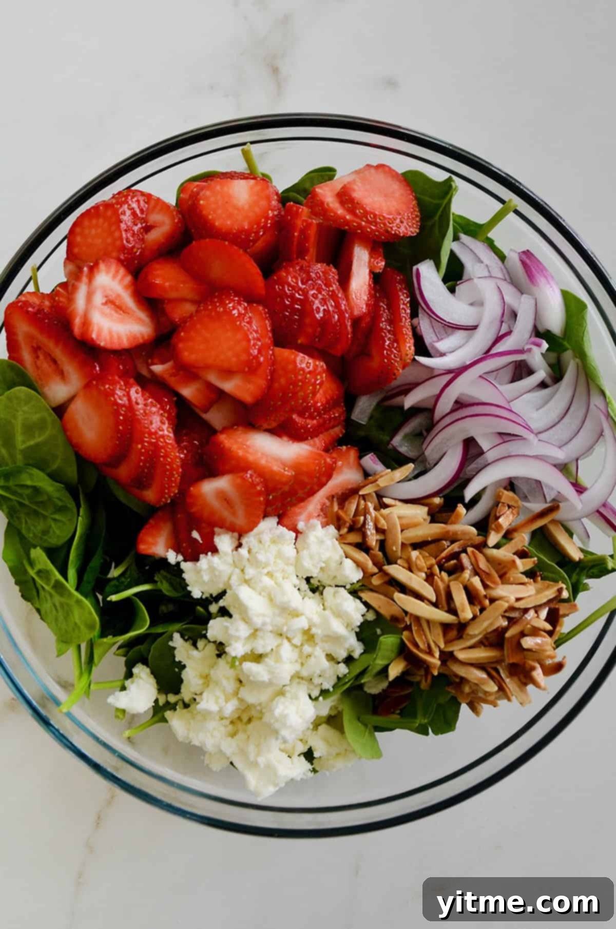 Spinach, strawberries, onions, nuts, and feta cheese in a glass bowl