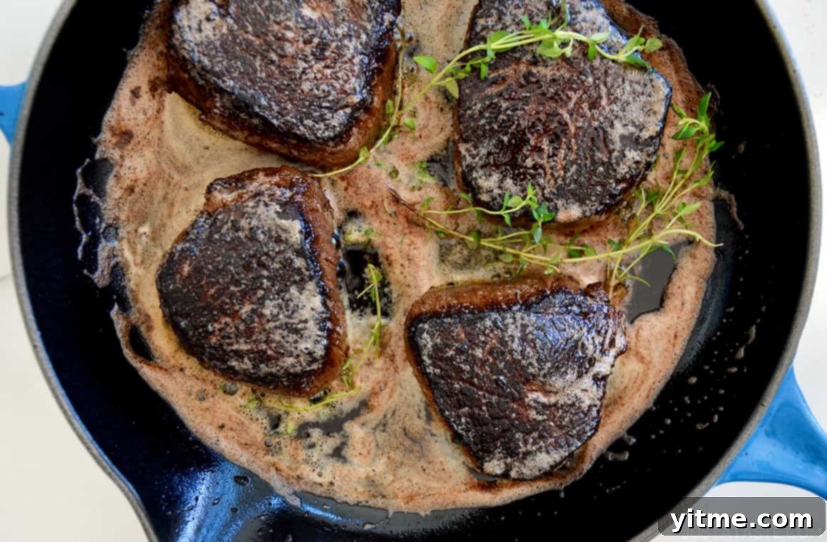 A skillet with juicy steaks, melting butter, and fresh thyme sprigs