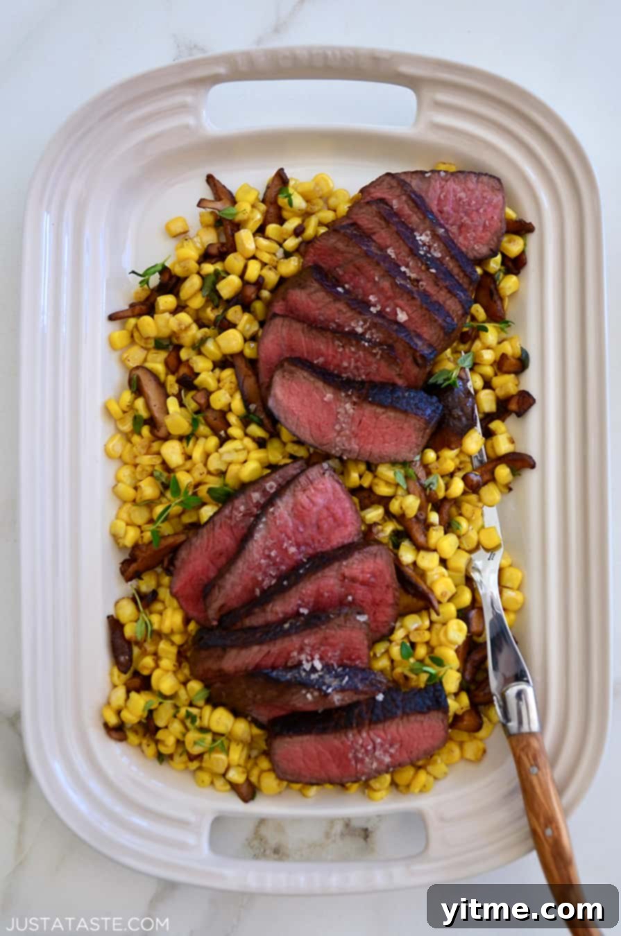 Slices of steak on a white platter, served over corn and mushrooms