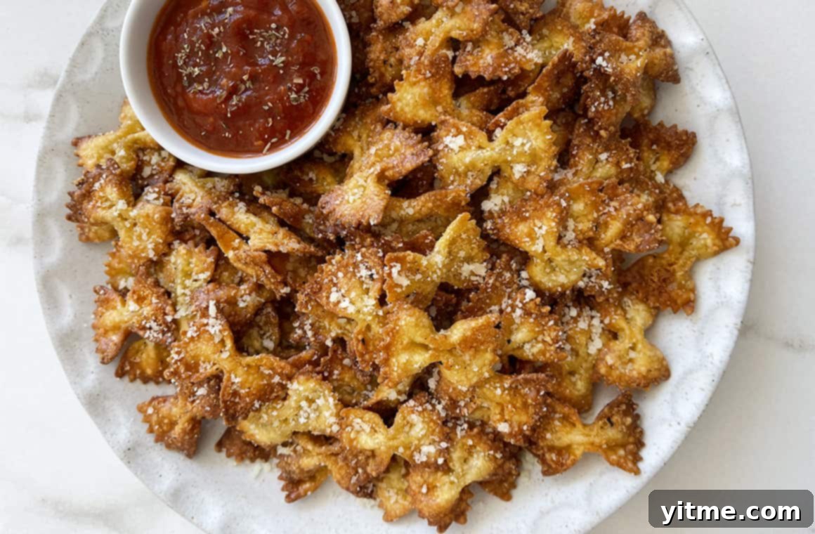 A white plate containing pasta chips topped with grated Parmesan cheese and fresh herbs