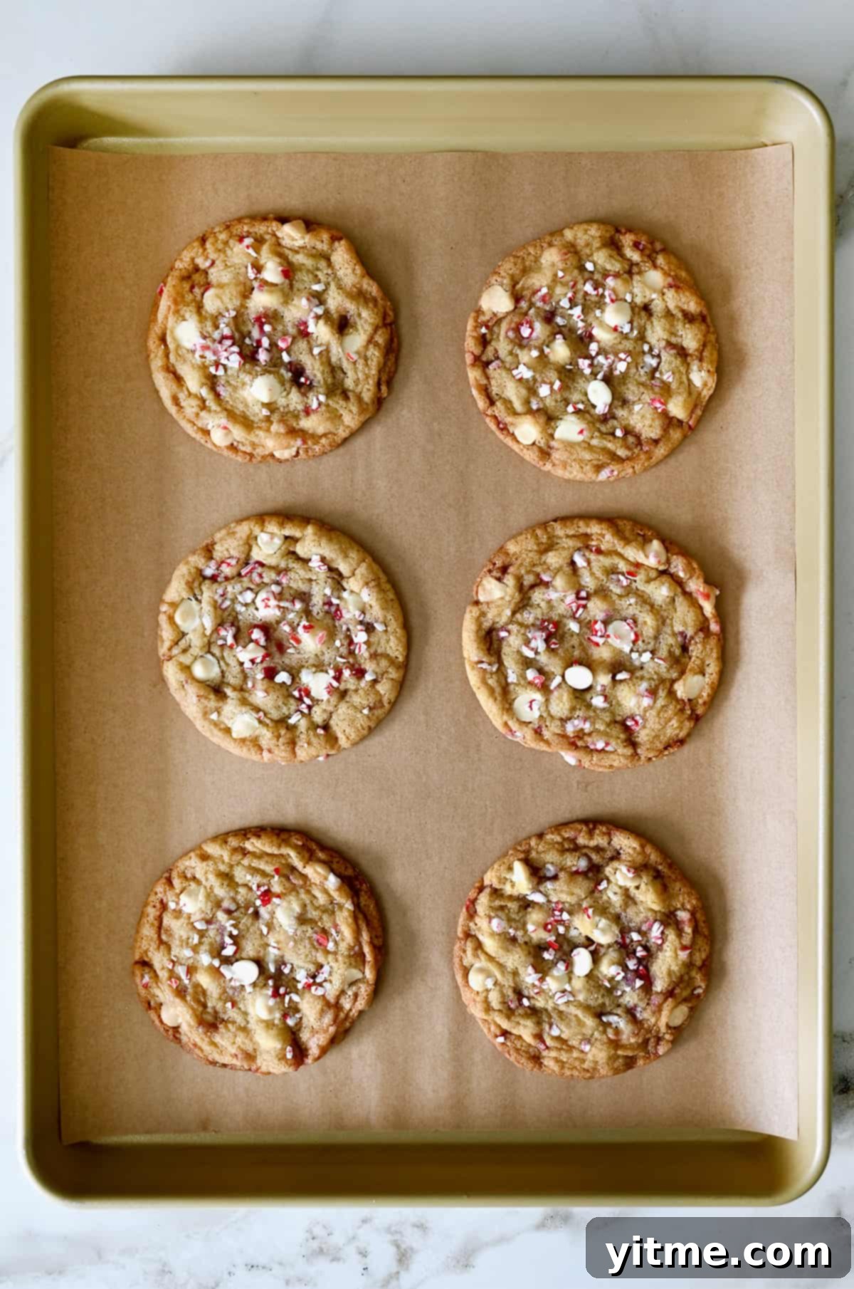 Six perfectly baked white chocolate peppermint cookies cooling on a parchment paper-lined baking sheet, showing their crisp edges and soft centers.