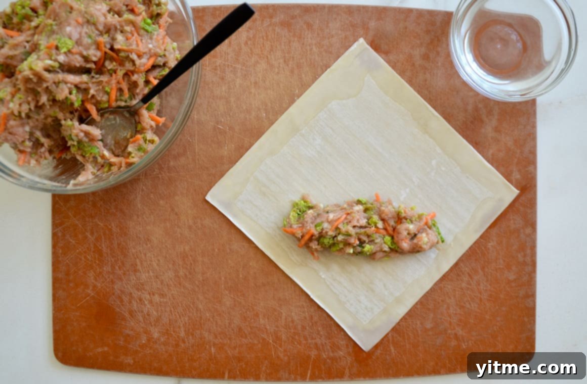 Ground chicken mixture atop a single egg roll wrapper, ready to be rolled into a delicious egg roll