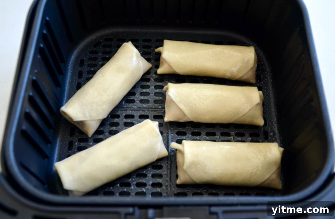 Perfectly arranged egg rolls nestled in an air fryer basket, ready for cooking