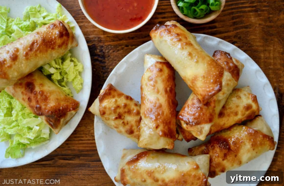 A plate of golden Air Fryer Egg Rolls next to a bowl of sweet chili sauce, ready to be devoured