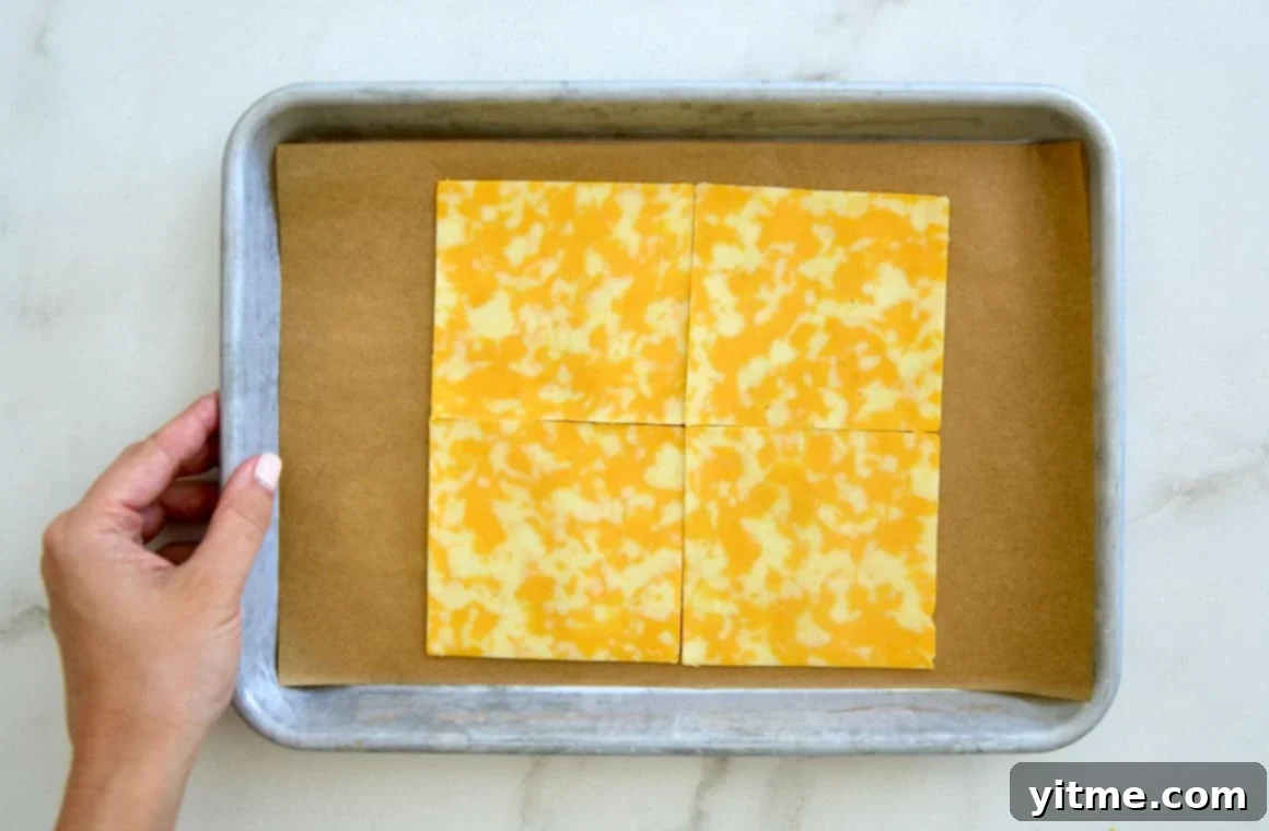 Cheesy Keto Wraps 3 Four slices of cheese arranged on parchment paper on a baking sheet