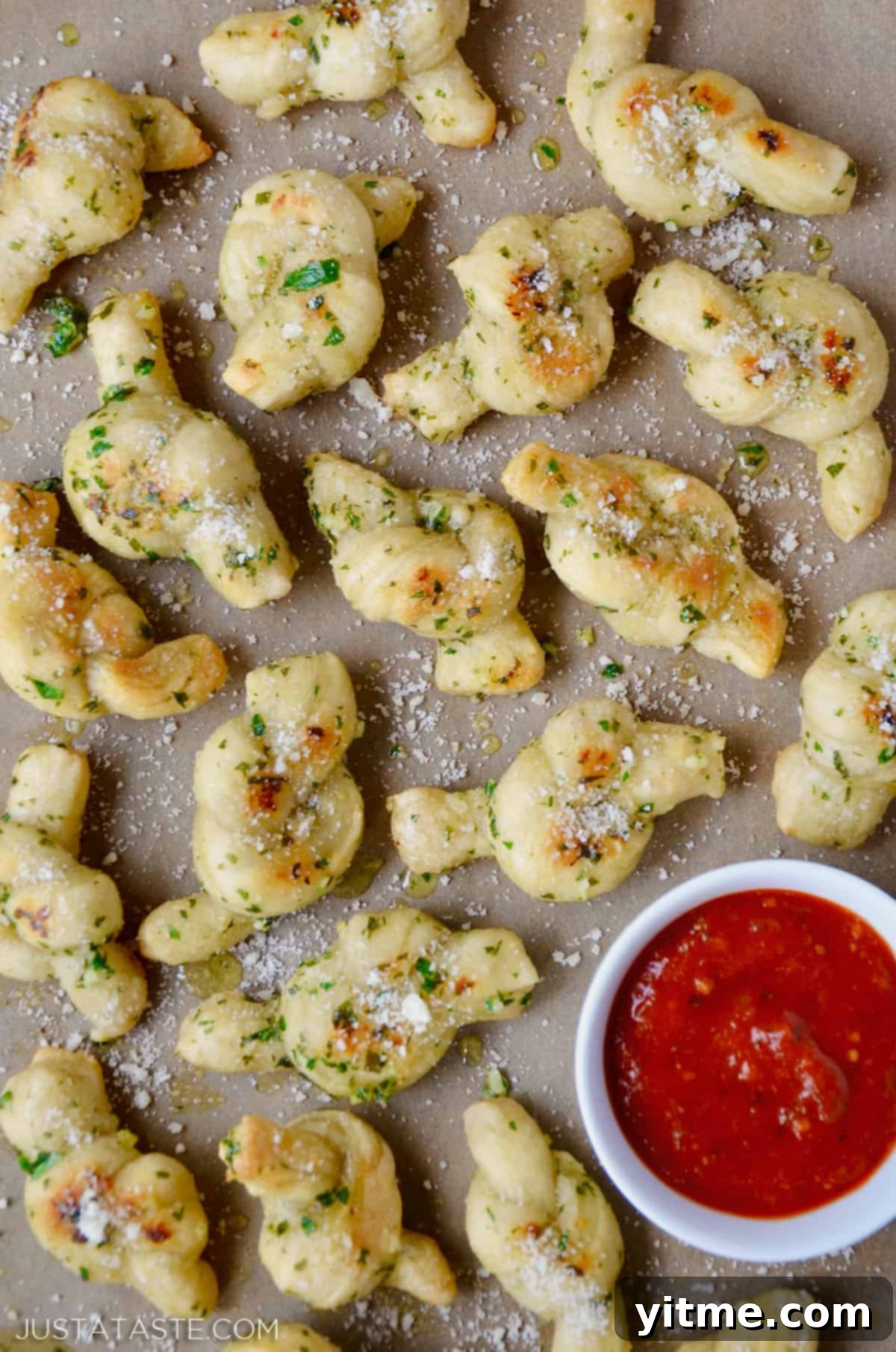 Speedy Garlic Knots: A Simple Recipe 2 Golden garlic knots sprinkled with Parmesan cheese, served alongside a bowl of vibrant marinara sauce.