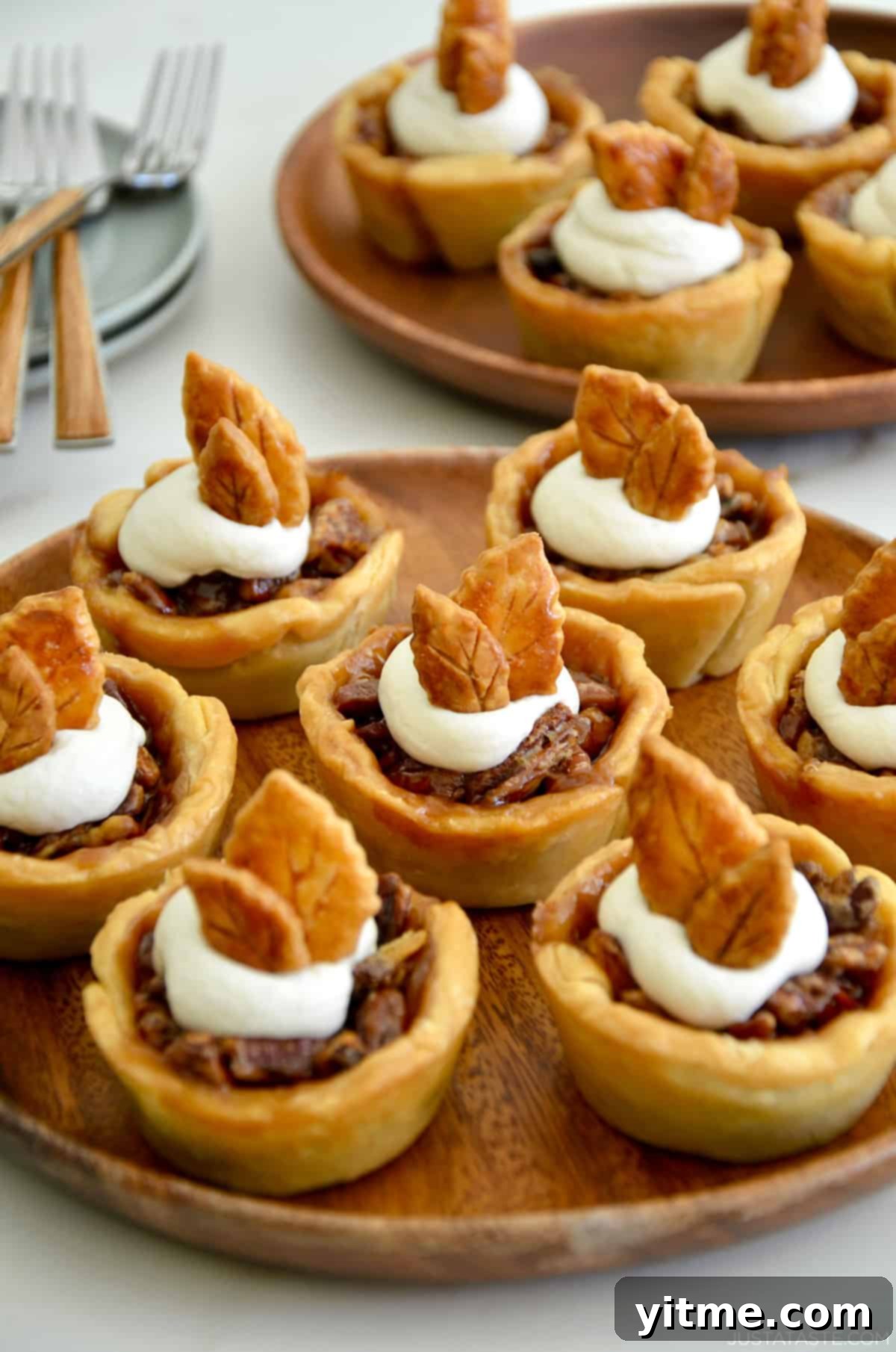Mini pecan pies topped with whipped cream and pie crust leaves on a white platter