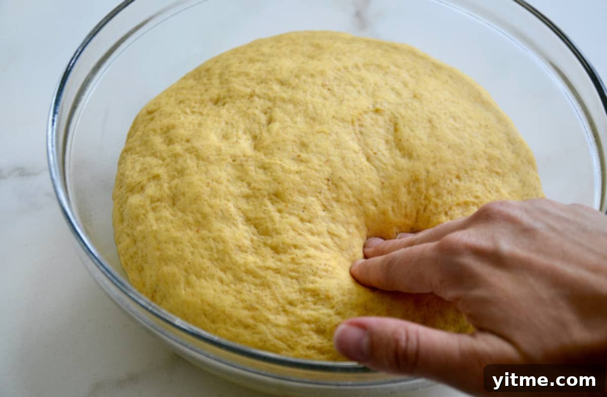 A hand pressing into a glass bowl containing proofed bread dough.