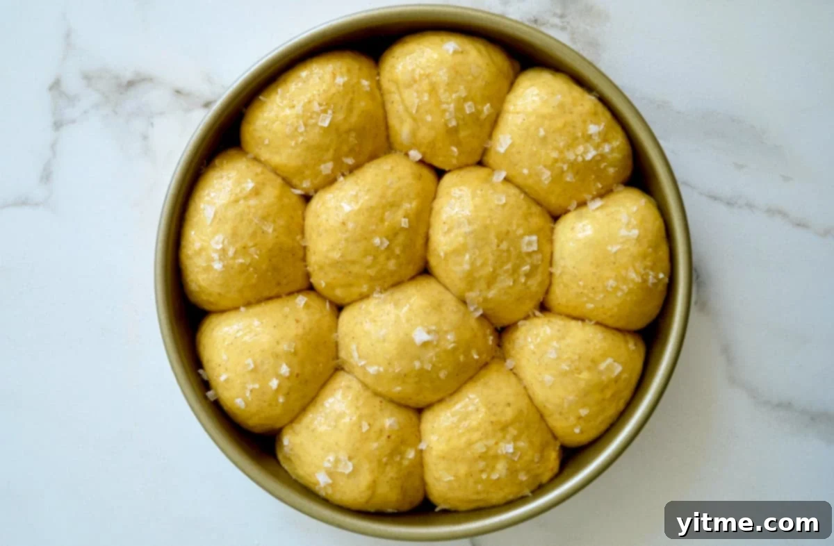 Unbaked pumpkin dinner rolls topped with large-flake sea salt in a round pan.