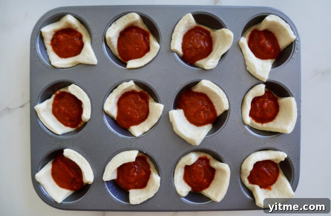 Muffin Tin Pizzas: Bite-Sized Fun 5 Muffin tin with dough and marinara sauce