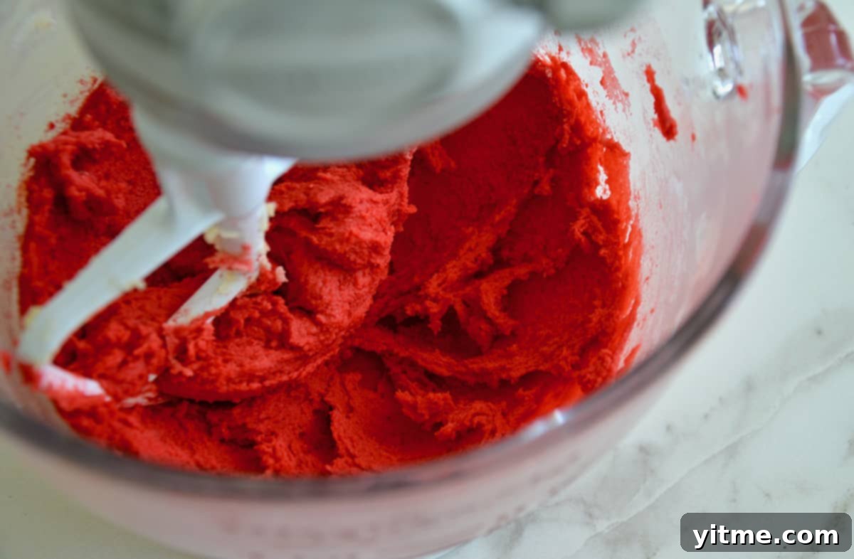 Red-colored sugar cookie dough in the bowl of a stand mixer.