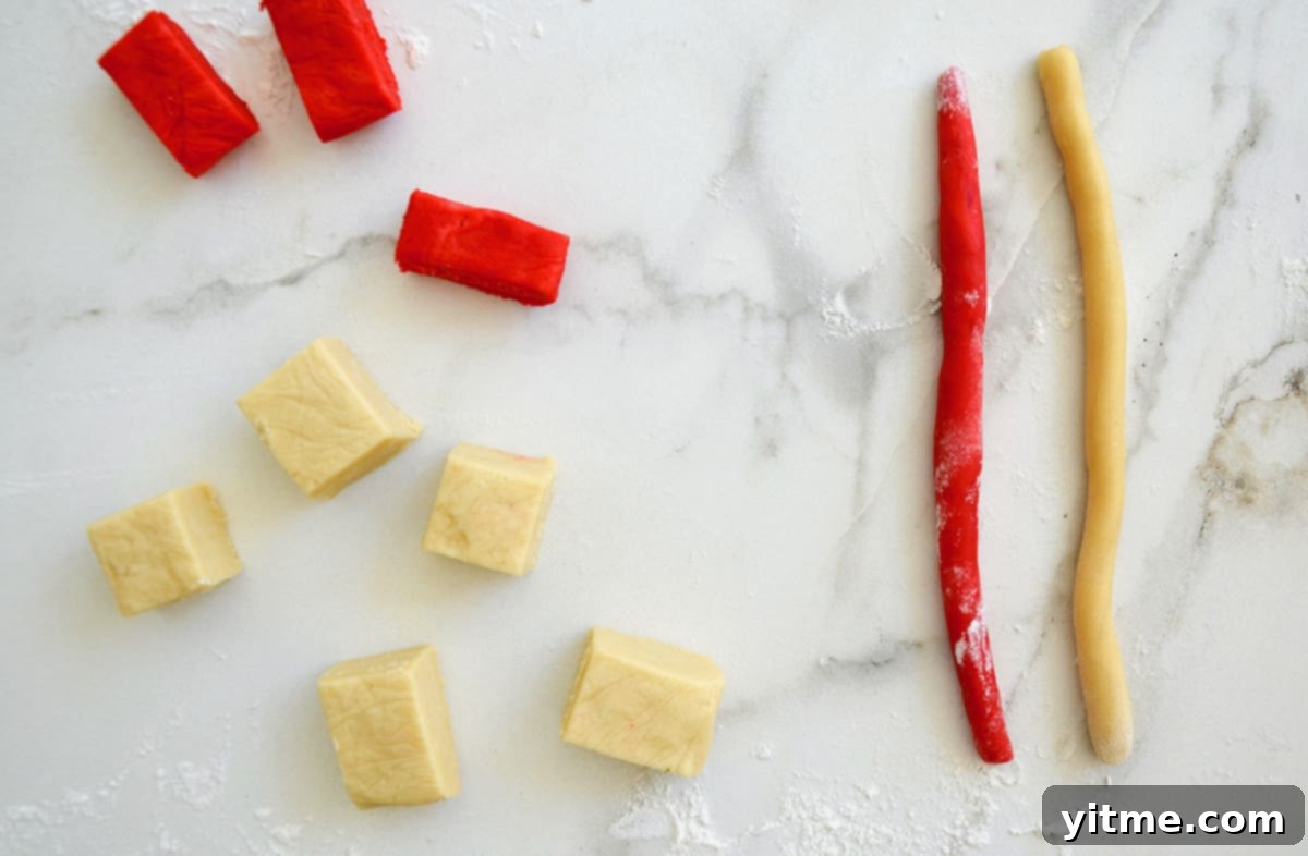 Red and plain-colored cookie dough, cubed and logged, laid out on a marble surface.