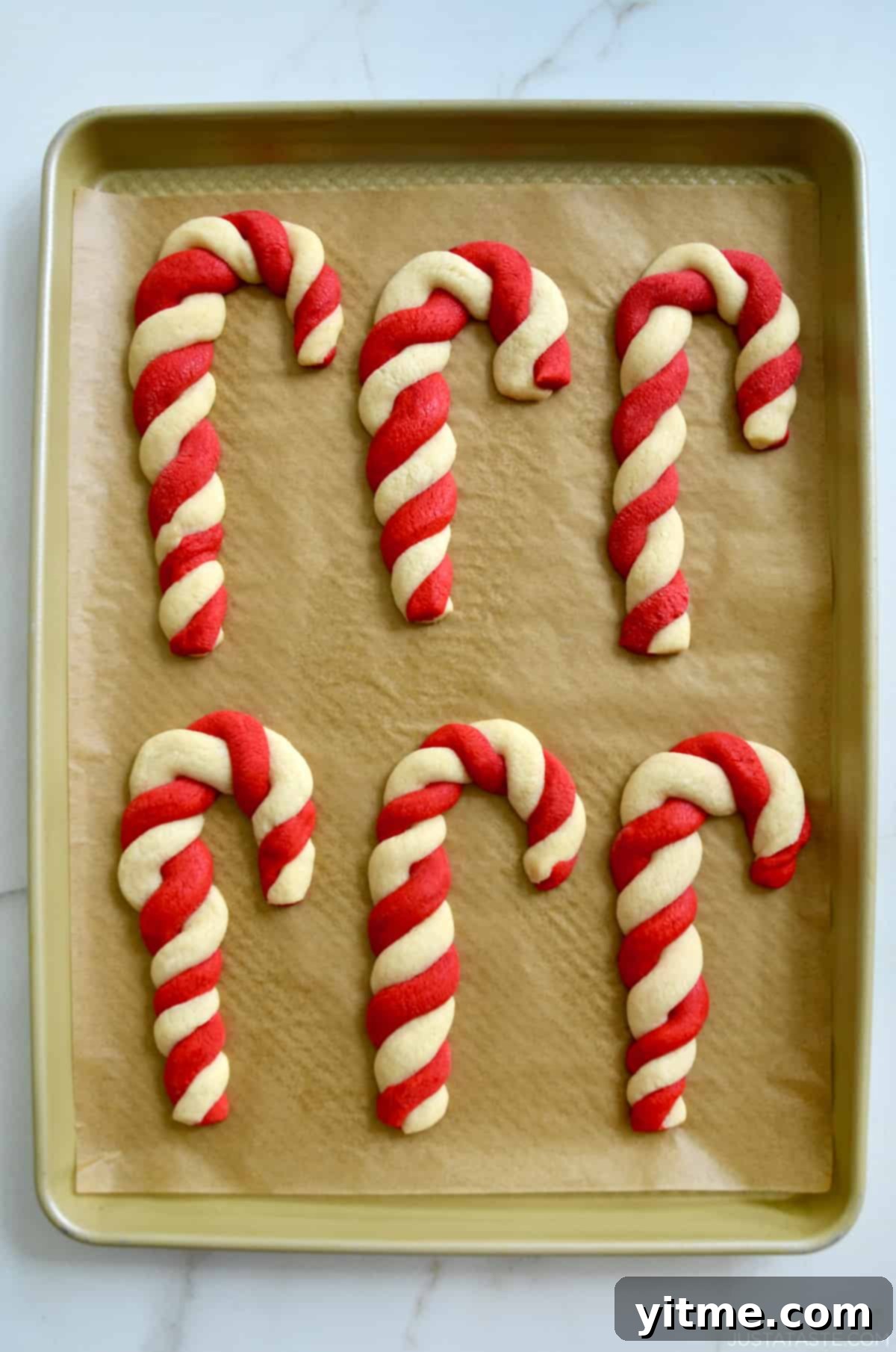 Freshly baked candy cane cookies on a parchment paper-lined baking sheet.