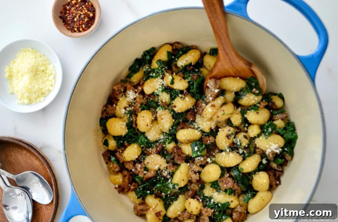 Quick A close-up view of One-Pot Gnocchi with Sausage and kale in a large stock pot next to small ramekins containing parmesan cheese and red pepper flakes for garnish.