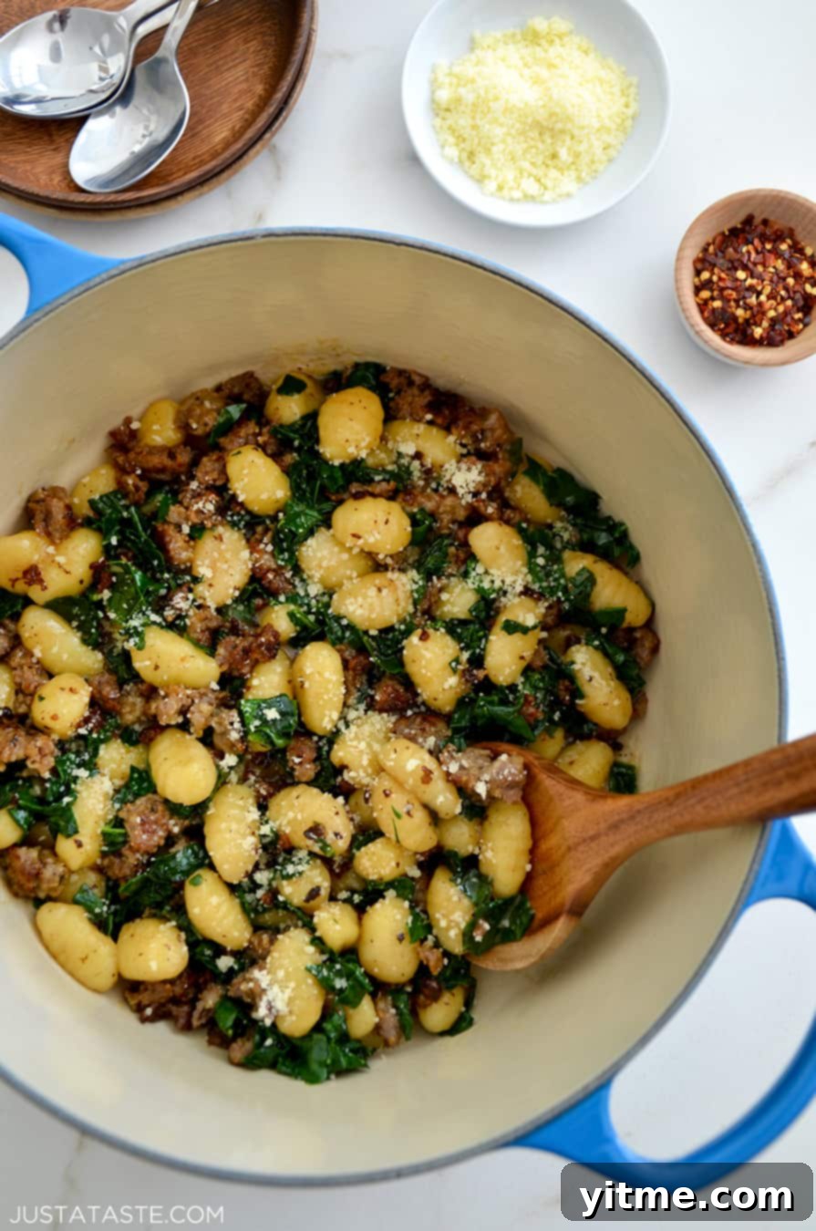 One-Pot Gnocchi with Sausage in a Dutch oven with a wooden spoon, garnished with fresh Parmesan and a sprinkle of red pepper flakes.