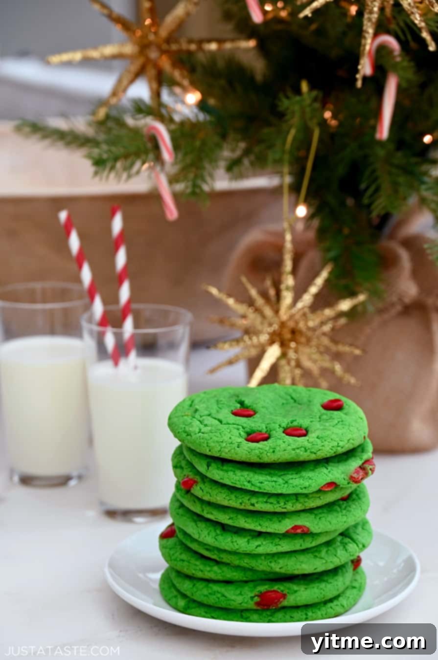 A tall stack of Cake Mix Grinch Cookies on a plate in front of two glasses of milk with straws