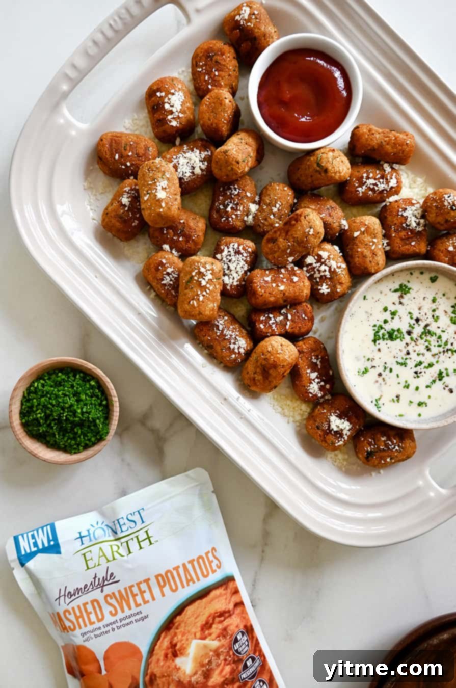 A platter of golden brown sweet potato tots with bowls of ketchup and Ranch dressing for dipping.