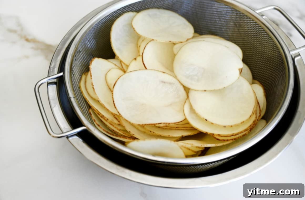 Thinly sliced potatoes soaking in an ice water bath to remove starch, a crucial step for crispy chips.