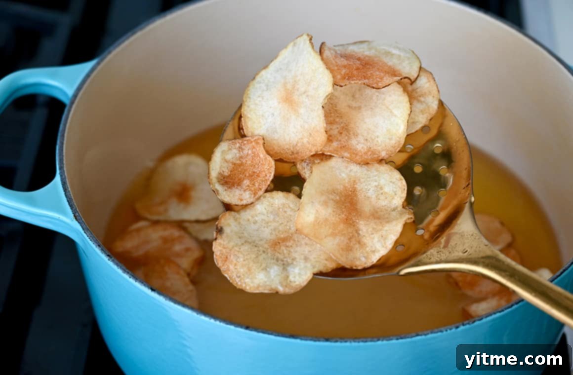 A slotted spoon lifts freshly fried golden potato chips from a large stockpot of hot oil, ready for seasoning.