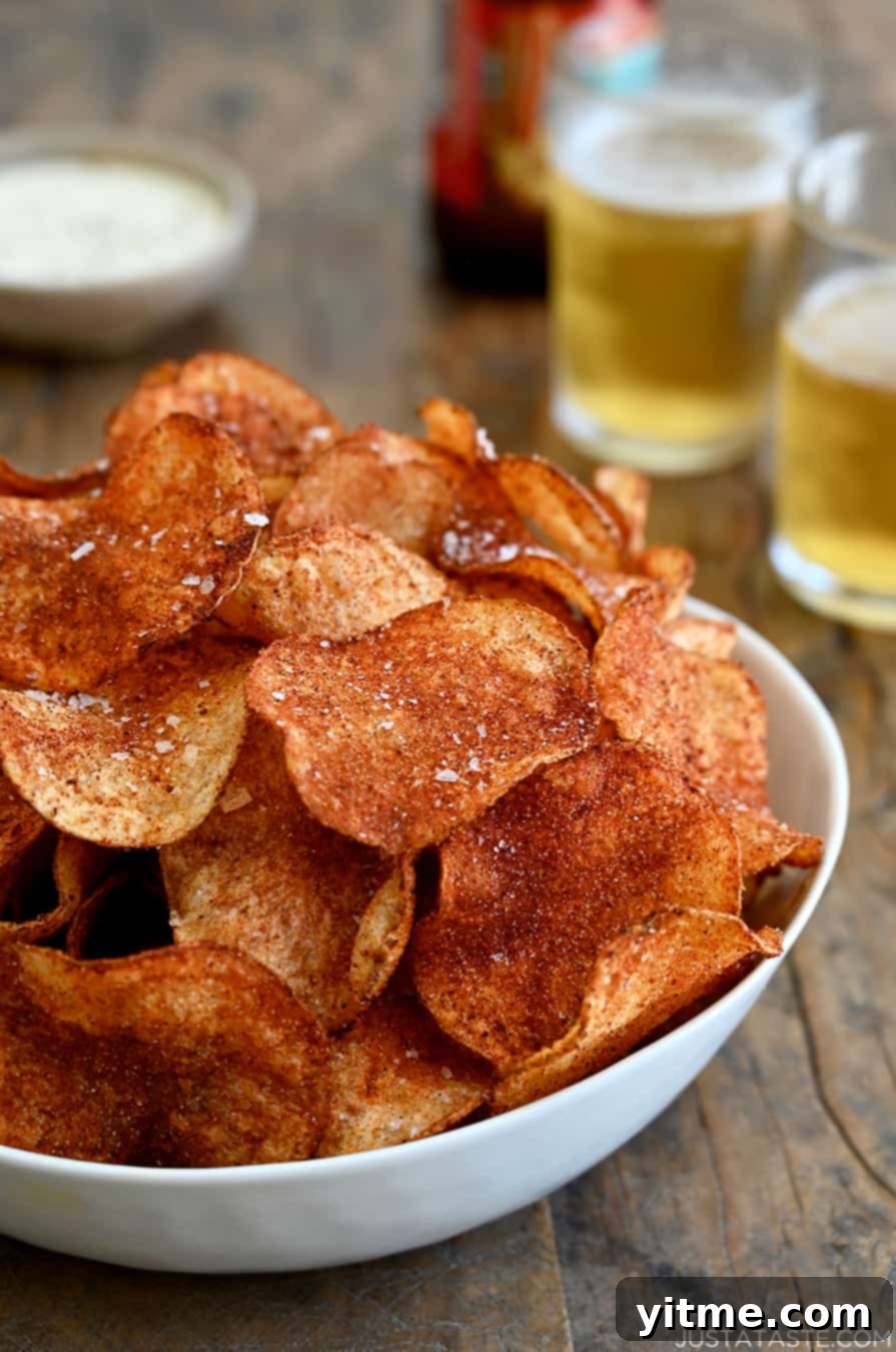 A white serving bowl containing Homemade Barbecue Potato Chips with two glasses filled with beer in the background