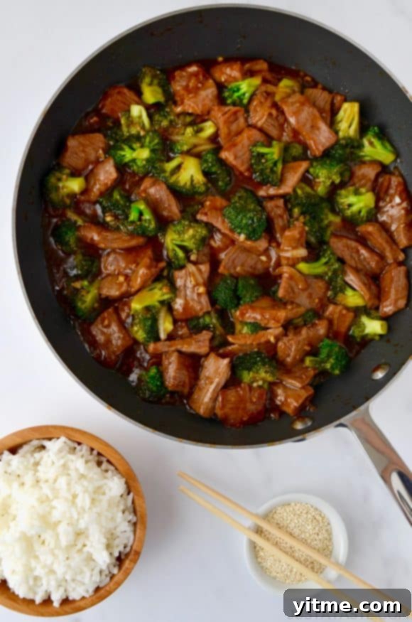 Top Recipes That Defined 2021 13 Easy Beef and Broccoli in a nonstick sauté pan, white rice in a small brown bowl and sesame seeds in a small white ramekin with chopsticks resting on top.