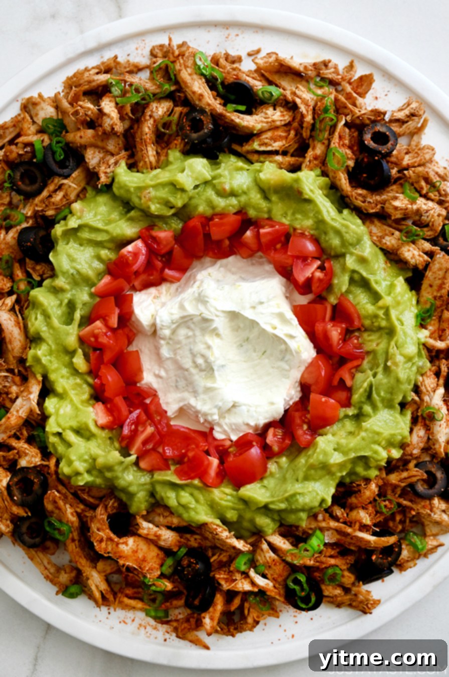 A close-up view of the creamy chicken taco dip featuring a vibrant cream cheese base, diced red tomatoes, fresh green guacamole, and dark sliced black olives.