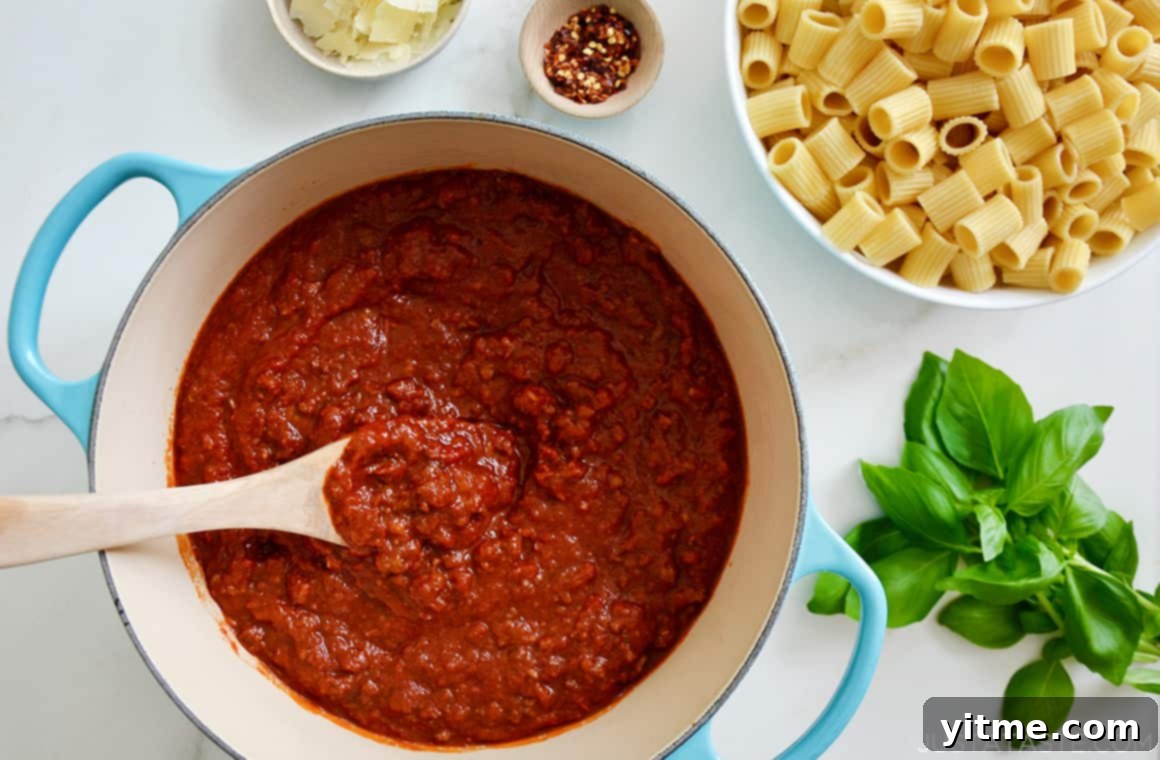 A bird's-eye view of homemade Bolognese sauce simmering in a large stock pot, next to a bowl of perfectly cooked rigatoni pasta, ready to be enjoyed.