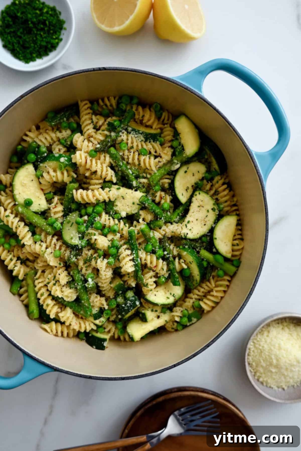 Pasta Primavera with peas, asparagus, and zucchini in a blue Dutch oven, with Parmesan and bowls nearby.