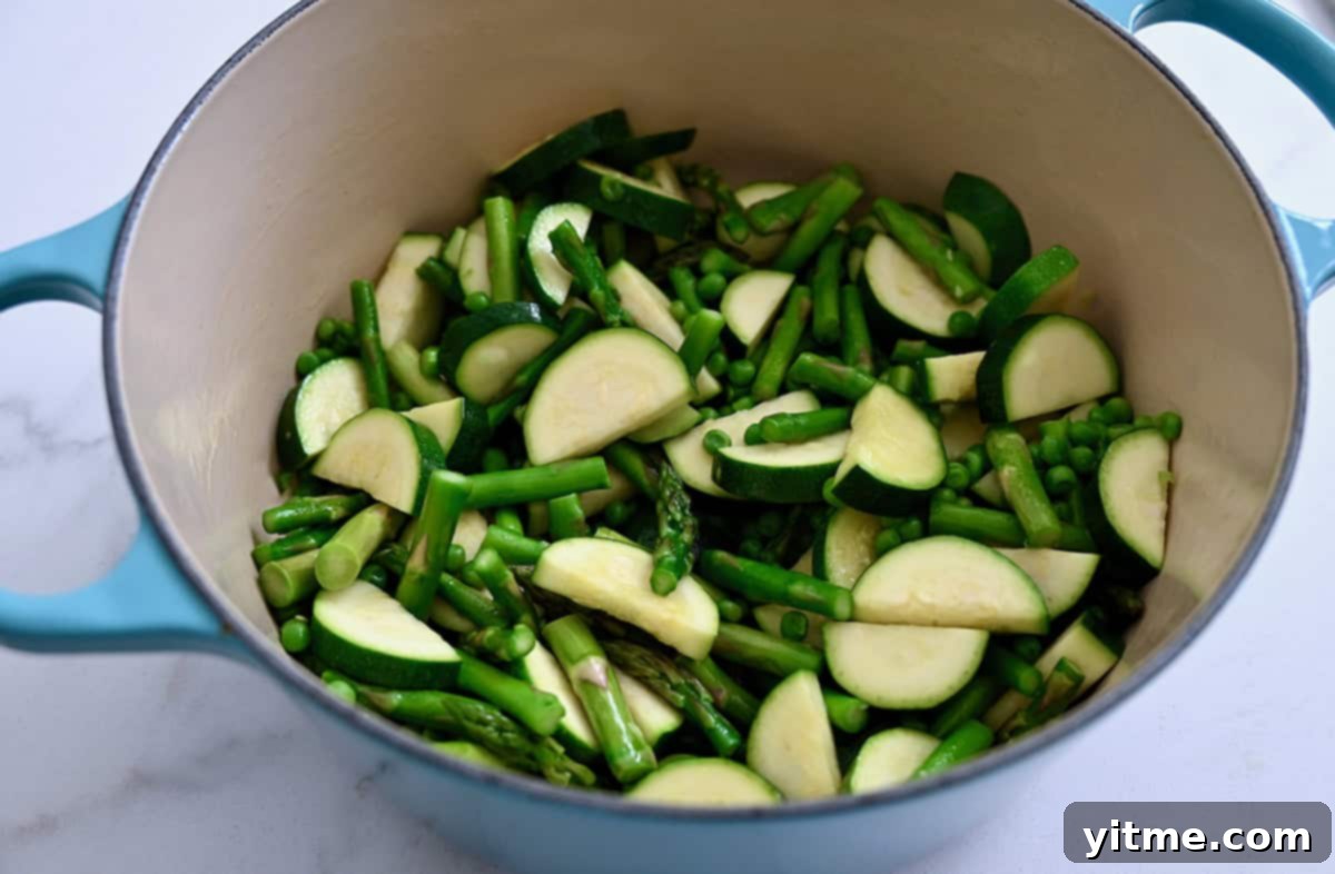Sautéed vegetables including peas, zucchini, and asparagus in a Dutch oven.