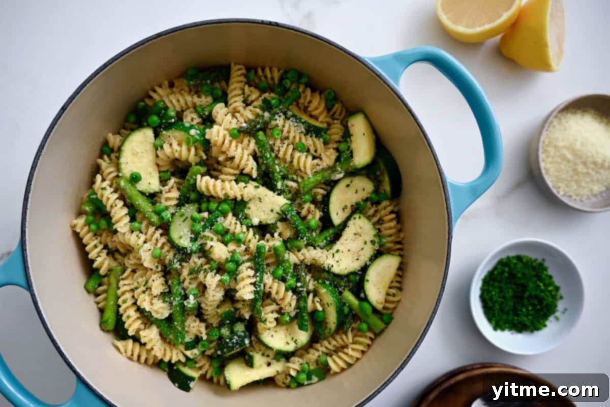 Pasta Primavera in a Dutch oven with Parmesan, chives, and lemon halves.