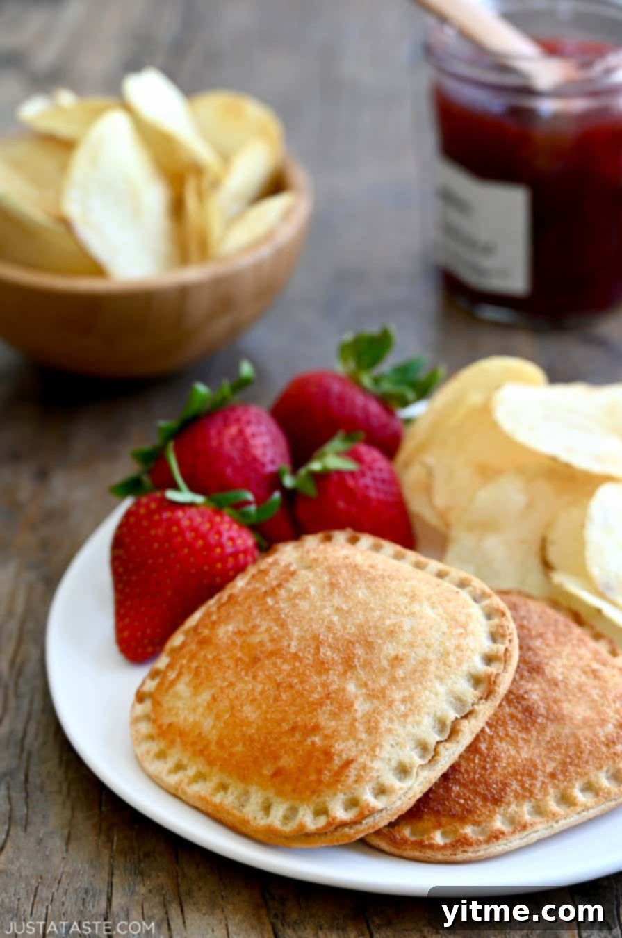 Warm and Gooey Air Fried PB&J 7 Air Fryer Peanut Butter and Jelly Uncrustables on a white plate with strawberries and potato chips