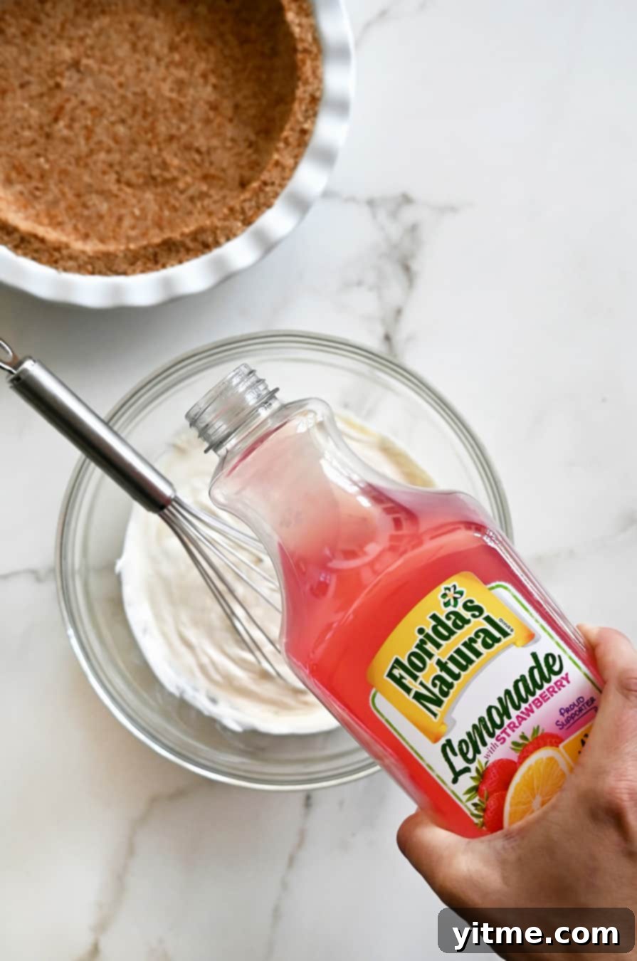 A bottle of Florida's Natural Strawberry Lemonade being poured into a clear glass bowl, illustrating the first step of making the creamy filling