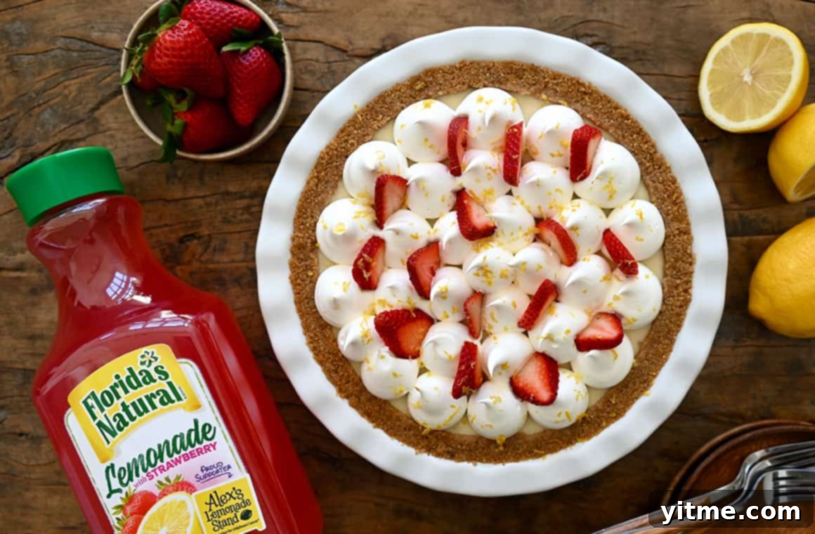 A top-down view of a complete Strawberry Lemon Icebox Pie with a bottle of strawberry lemonade and fresh strawberries arranged artfully next to it