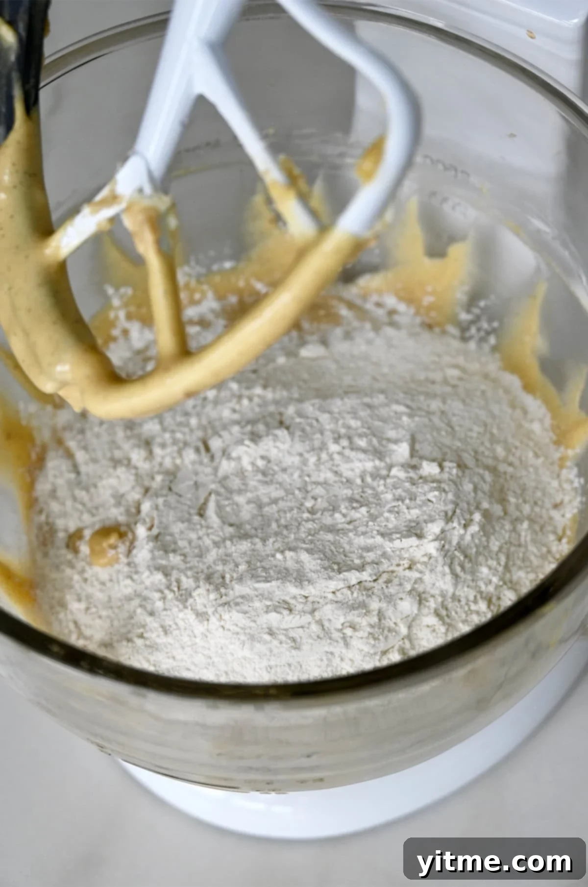A flour mixture sits atop creamed wet ingredients in the bowl of a stand mixer, ready to be combined into chewy chocolate chip cookie dough.