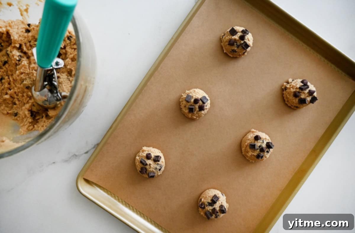 Six perfectly scooped mounds of chocolate chip cookie dough arranged on a parchment paper-lined baking sheet, ready for the oven.