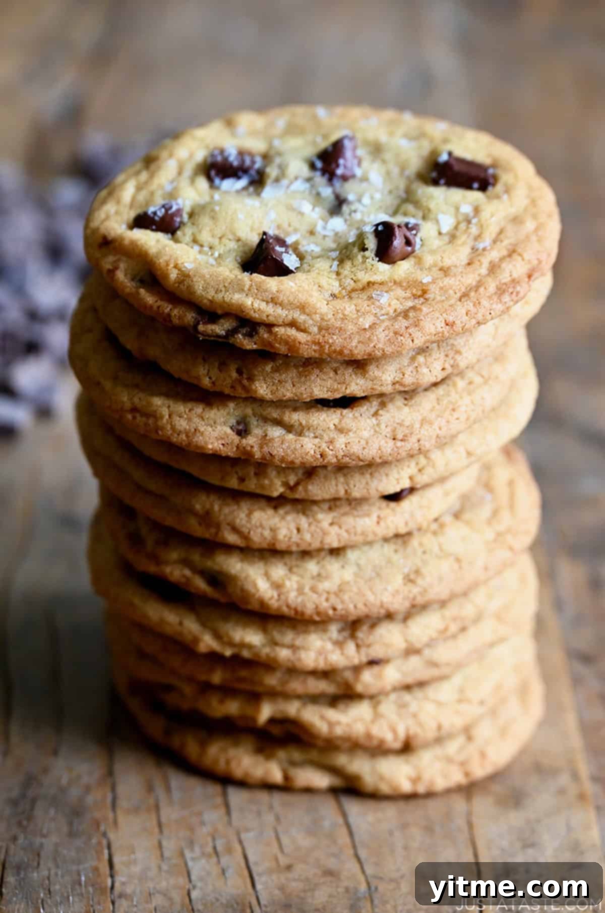 A tall stack of ten chewy chocolate chip cookies, indicating their soft texture and perfect golden-brown edges.
