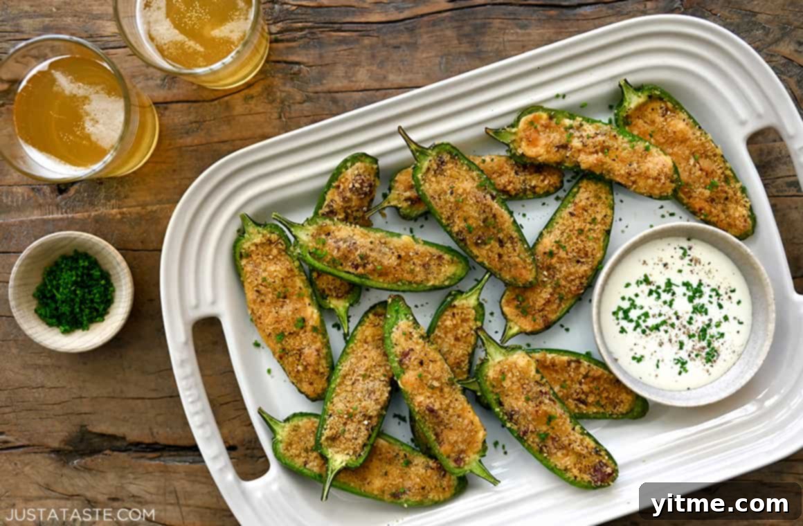 A top-down view of two glasses of beer next to a white serving platter piled high with golden Air Fryer Jalapeño Poppers with Bacon and a small bowl containing Ranch dipping sauce, ready for serving