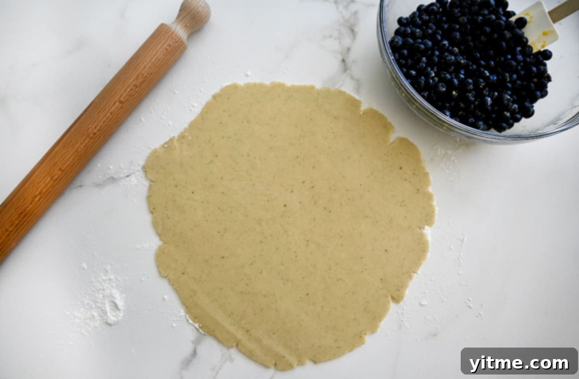 Rustic Blueberry Tart with Honey-Thyme Drizzle 5 Overhead view of rolled-out pie dough alongside a rolling pin and a clear bowl filled with berries.