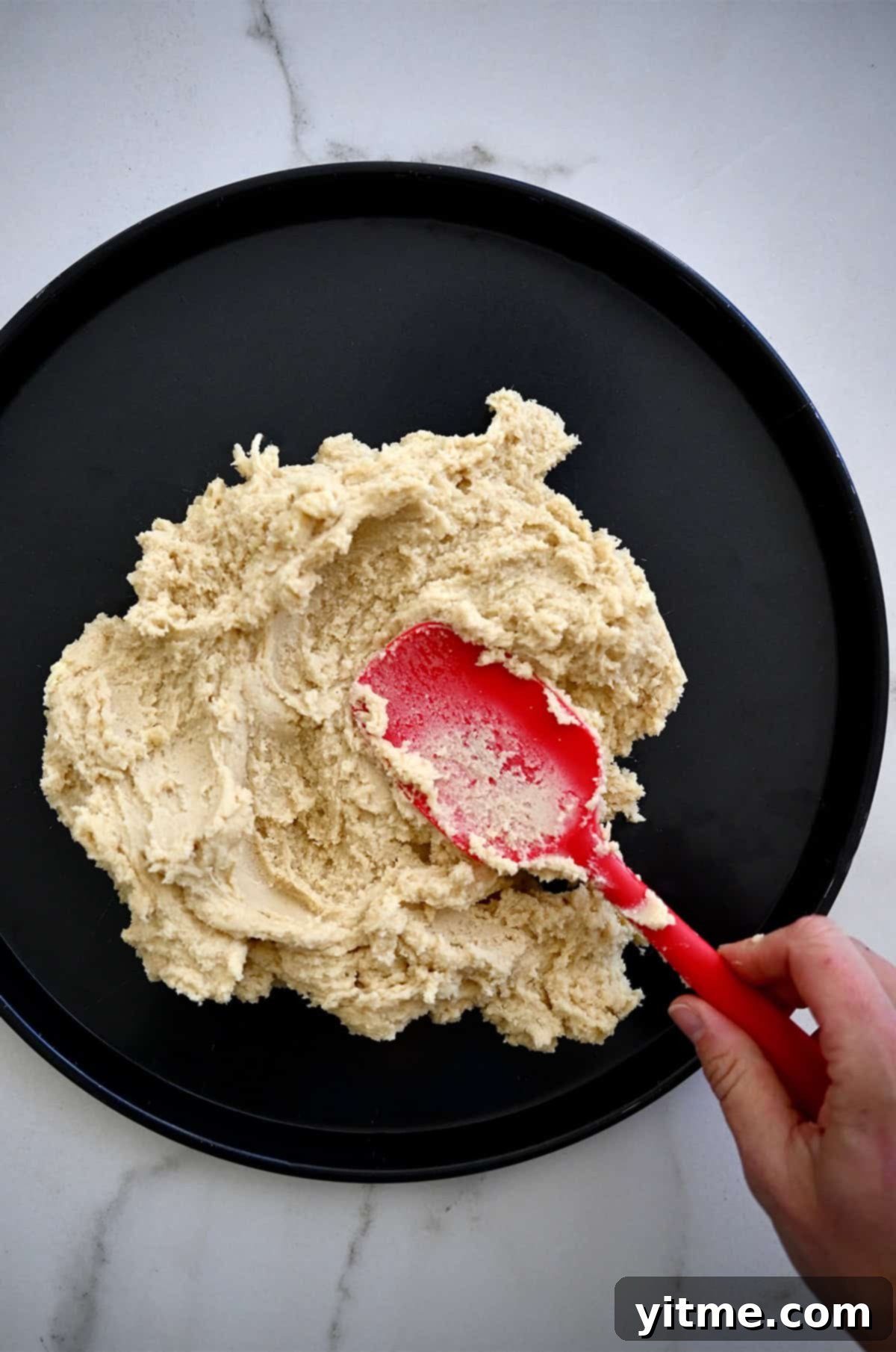Spreading sugar cookie dough onto a pizza pan with a spatula.