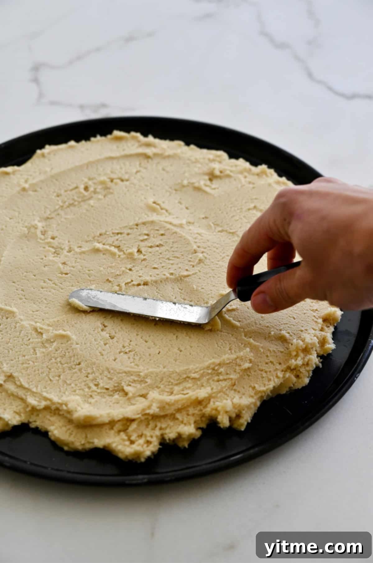 Spreading sugar cookie dough into a circle on a pizza pan.