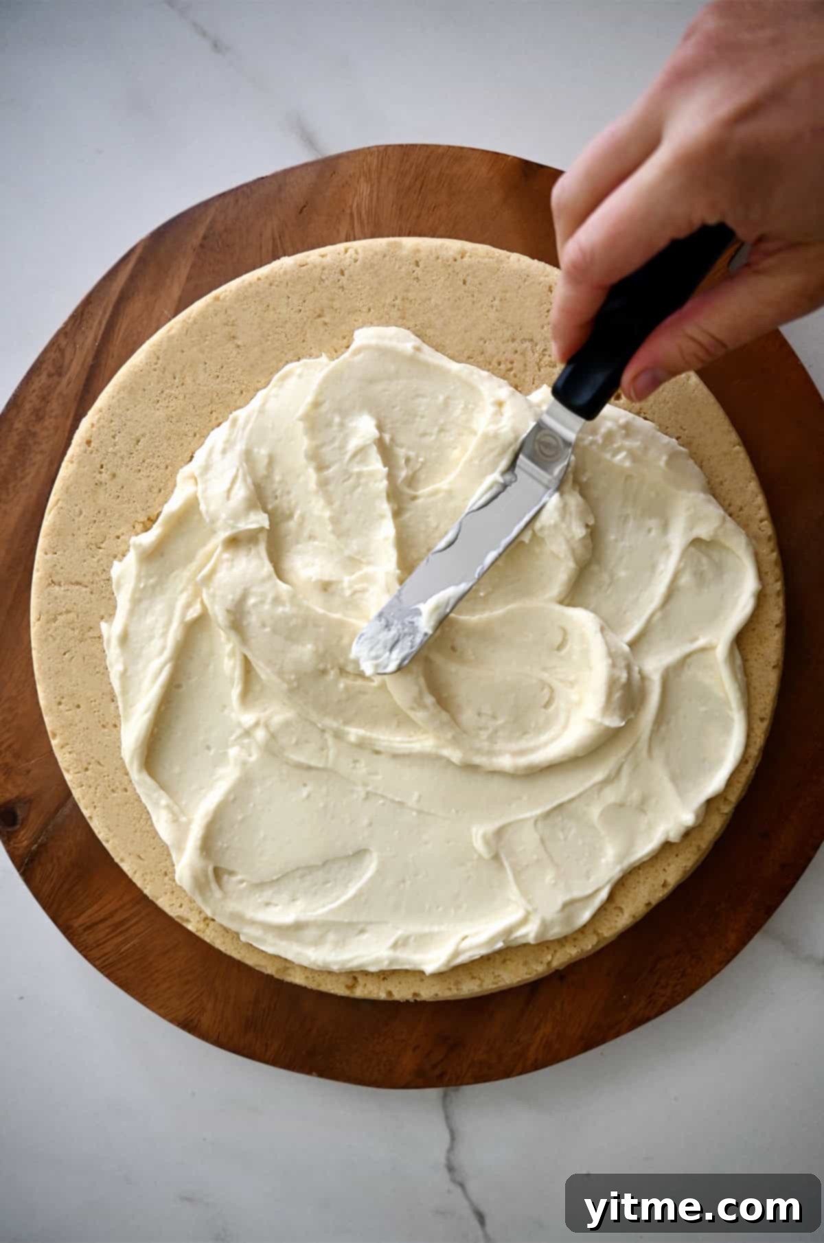 Spreading cream cheese frosting on a sugar cookie crust.