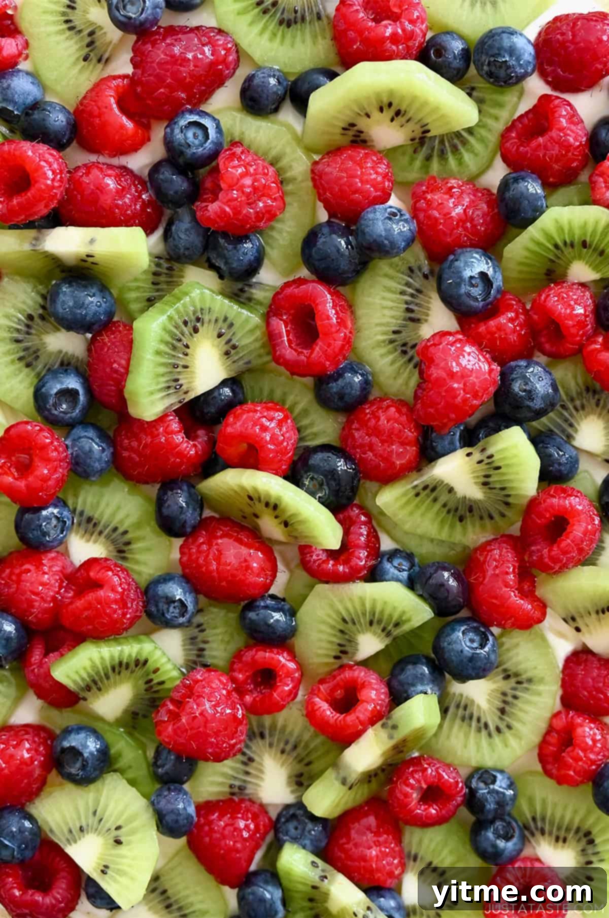 Fresh raspberries, blueberries, and kiwi slices on top of cream cheese frosting and a sugar cookie crust.
