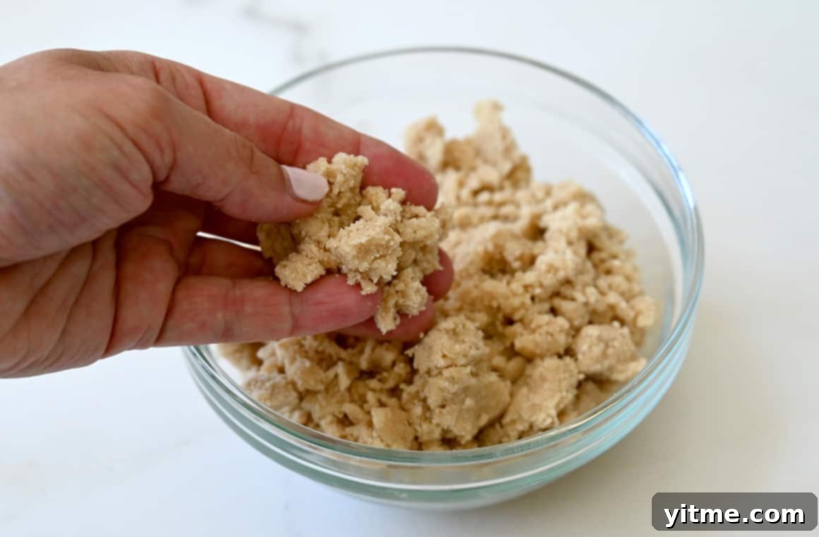 Streusel-Topped Cherry Pie Bites 6 A hand holding streusel topping over a small bowl containing even more streusel, ready to be sprinkled on the pies.