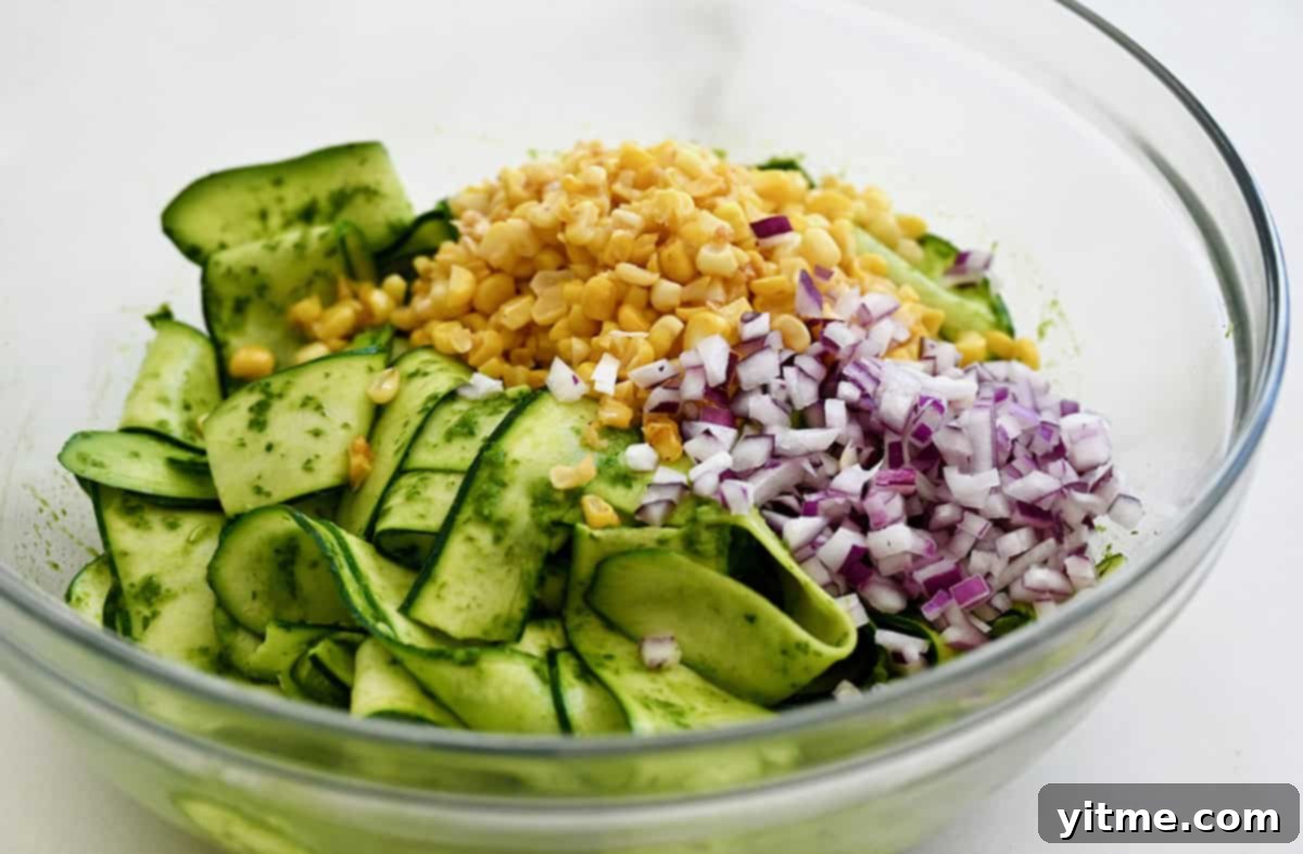 Zucchini ribbons, diced red onion, corn kernels, and basil vinaigrette in a mixing bowl.