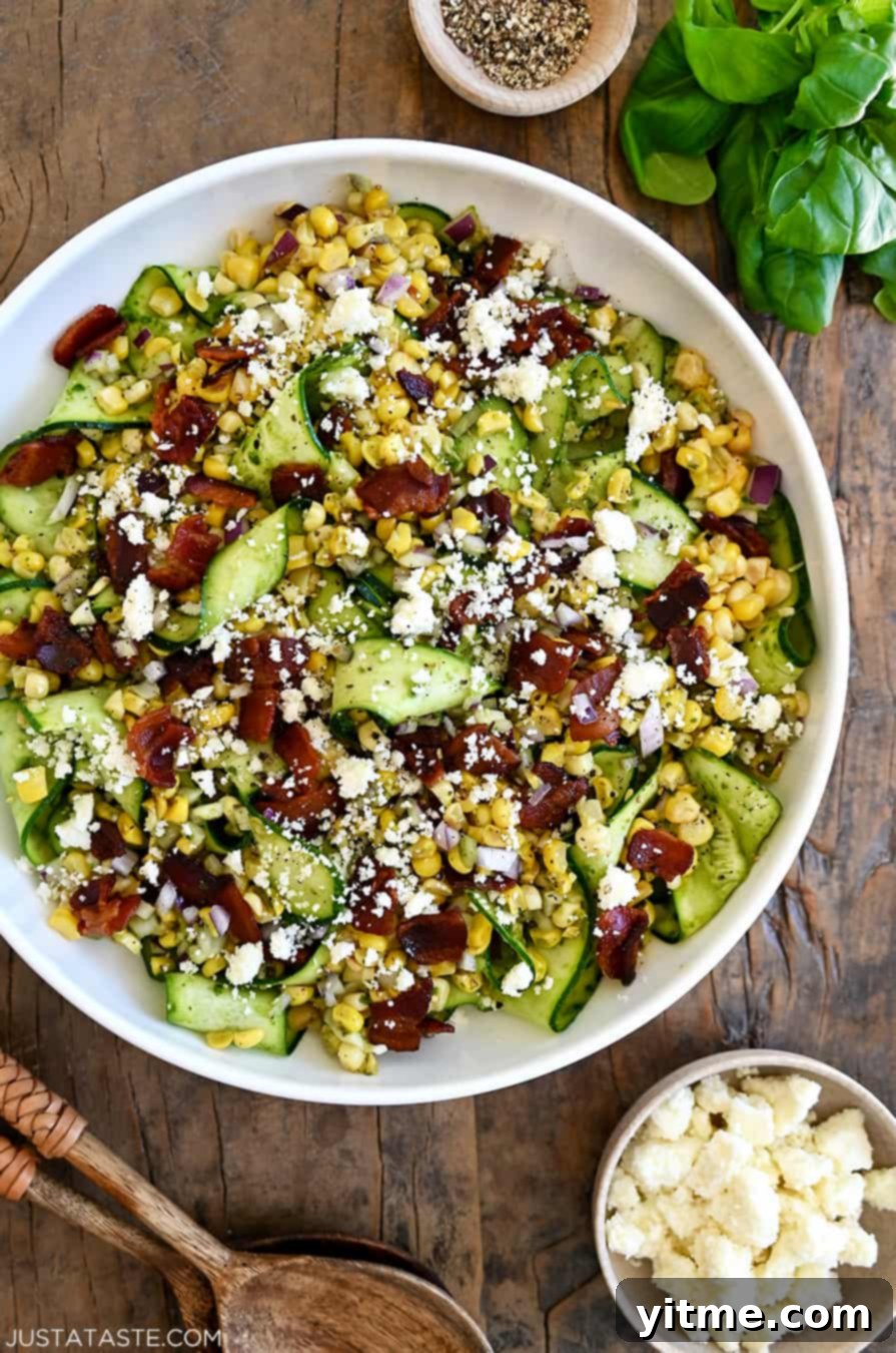 A top-down view of Corn and Zucchini Salad with Basil Vinaigrette in a large white serving bowl next to a small bowl filled with cotija cheese