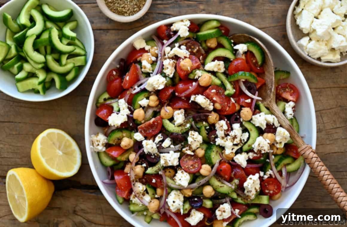 A serving bowl filled with Greek Cucumber, Tomato, and Chickpea Salad, garnished with black olives and feta cheese, accompanied by a wooden spoon