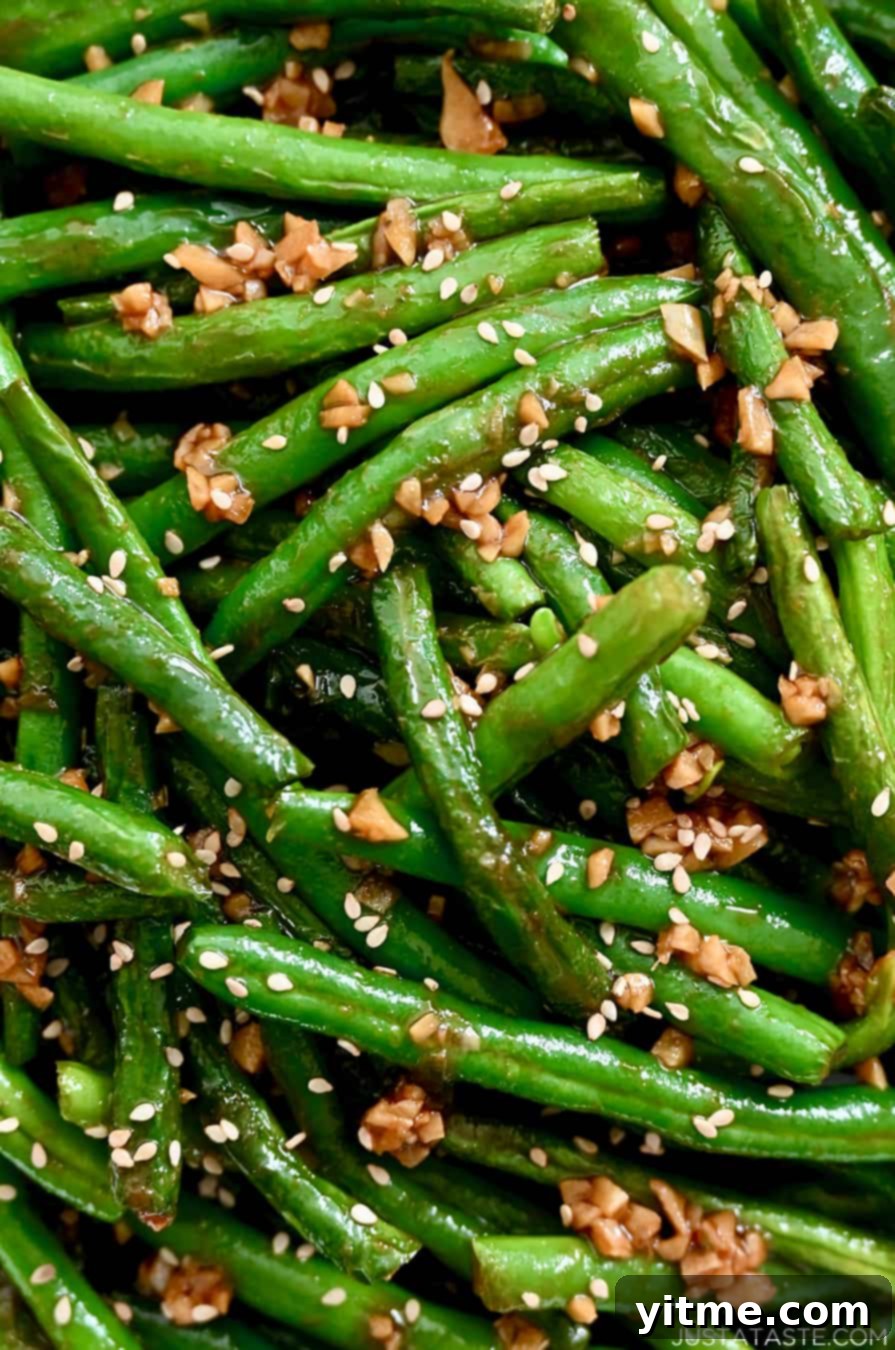 A close-up view of perfectly cooked copycat Din Tai Fung Chinese Garlic Green Beans in a white bowl, showing their beautiful blistered texture.