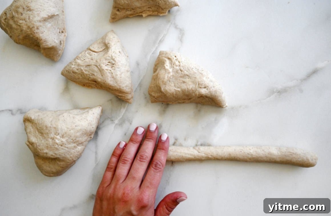 A hand rolls dough into a long log next to more dough pieces
