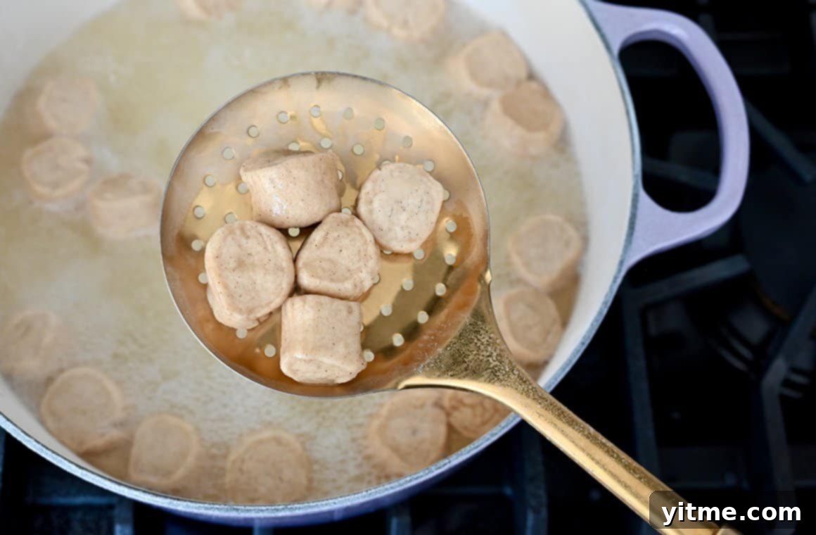 A slotted spoon with dough pieces over a large pot containing water and baking soda
